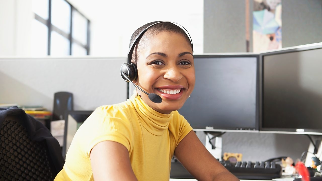 Mujer con camisa amarilla sentada sonriendo con sus auriculares puestos