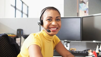 Mujer con camisa amarilla sentada sonriendo con sus auriculares puestos