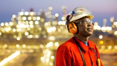 Un trabajador orgulloso, protegido por un casco, protectores auditivos y lentes de seguridad, luce esperanzado en una planta energética.