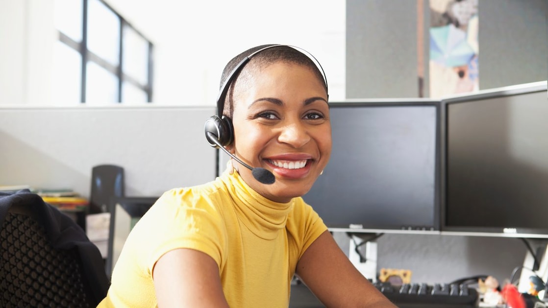 Mujer con camisa amarilla sentada sonriendo con sus auriculares puestos