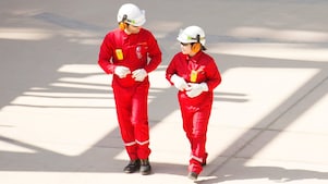 Trabajador y trabajadora con uniformes rojos, cascos blancos y protección auditiva caminando