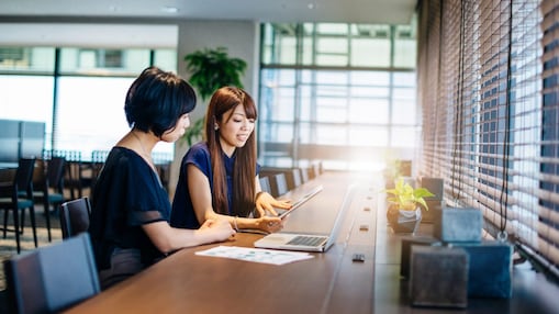 Dos mujeres sentadas en un escritorio mirando una computadora y una tableta