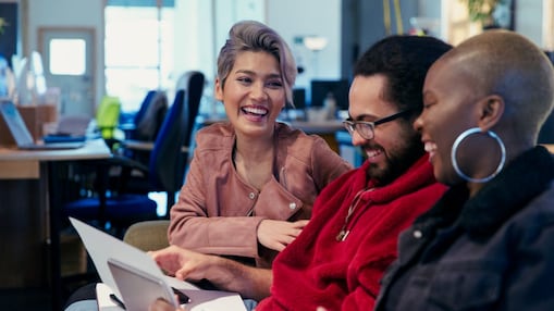 Tres personas en una oficina sentadas juntas, mirando papeles y riendo