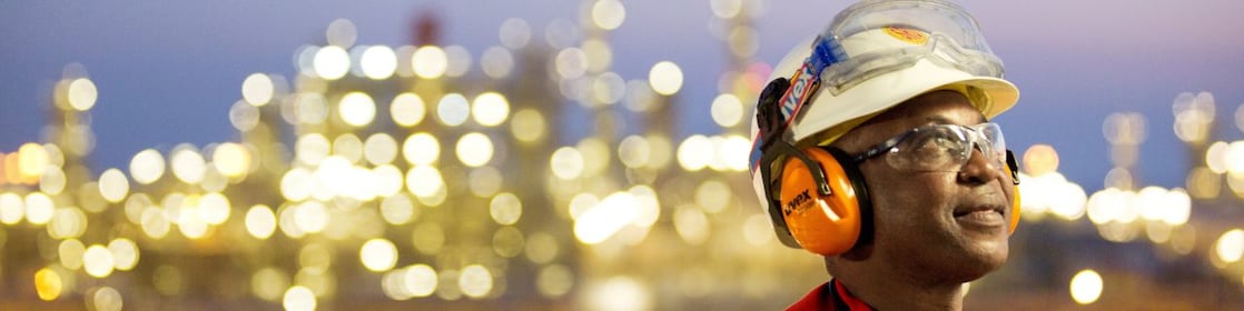 Un trabajador orgulloso, protegido por un casco, protectores auditivos y lentes de seguridad, luce esperanzado en una planta energética.