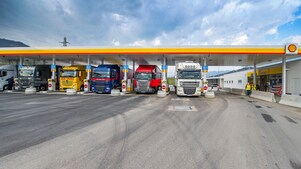 Gasolinera Shell con seis camiones aparcados. De izquierda a derecha: un camión blanco, verde oscuro, amarillo, azul oscuro, rojo y otro camión blanco.