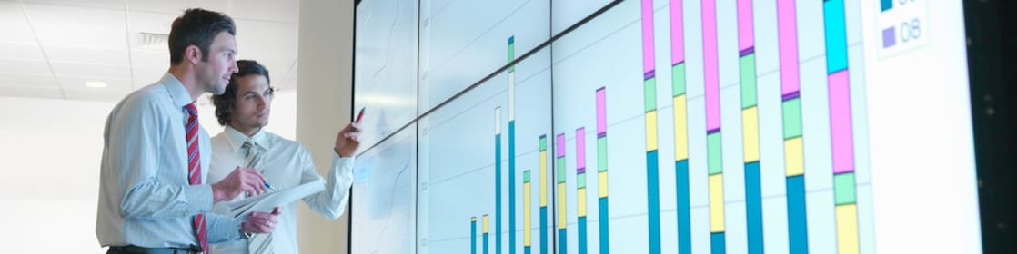 Hombres de negocios analizan informes visualizados en una gran pantalla digital