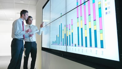 Hombres de negocios analizan informes visualizados en una gran pantalla digital